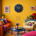 A vibrant living room with a yellow wall, featuring a large navy blue clock, colorful artwork, and an orange sofa. A blue coffee table holds a pink vase and a bowl of lemons. The text "ART STUDIO 39" is visible.