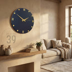 A navy blue wall clock with gold accents, including Roman numerals and dot markers. The clock hands are gold. The image also shows a shelf with vases, books, and a small plant, with the text "ART STUDIO 39".