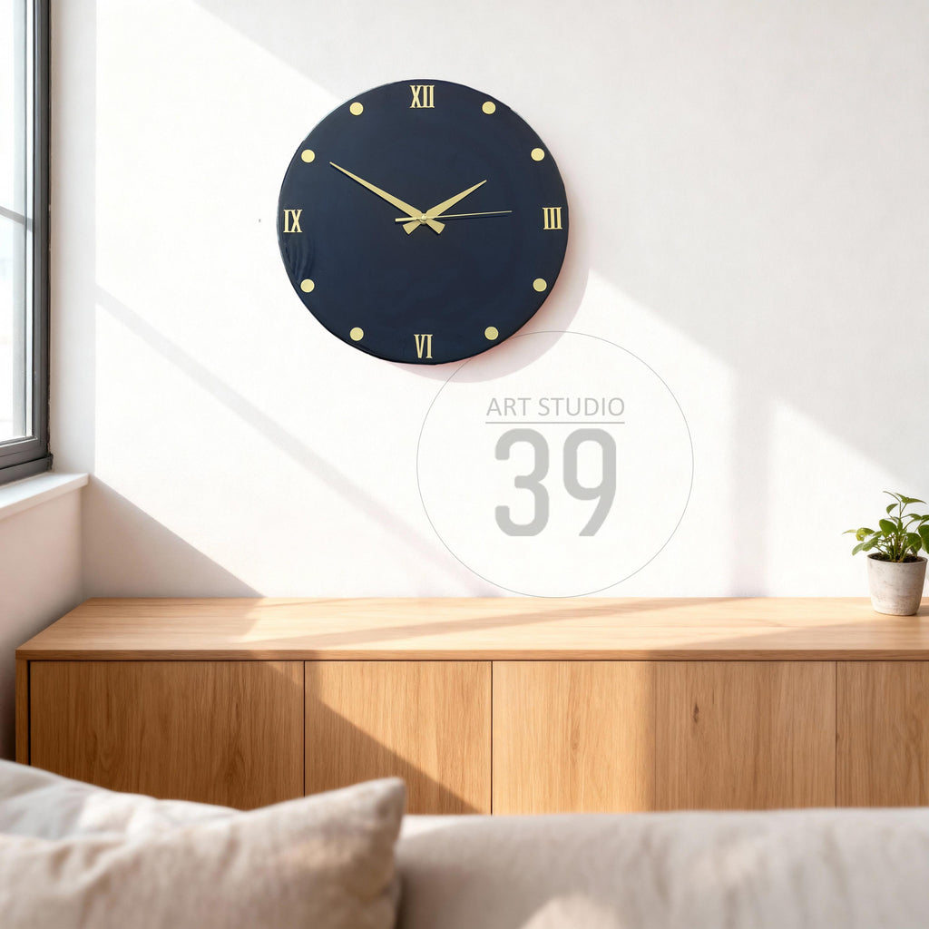 A navy blue wall clock with gold-colored Roman numerals and hands. The clock is round and mounted on a white wall. The clock is above a wooden cabinet. The text "ART STUDIO 39" is in the background.