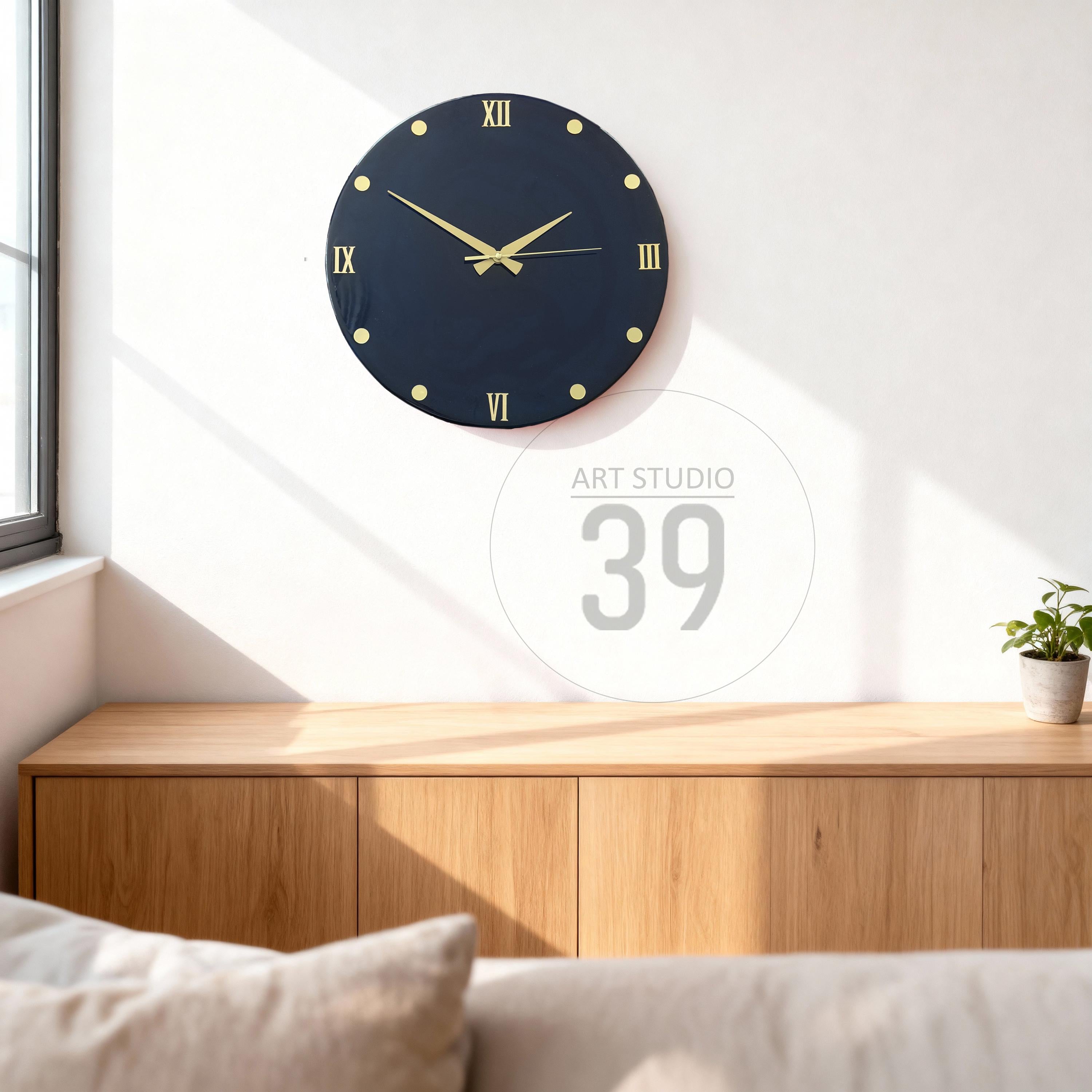 A navy blue wall clock with gold-colored Roman numerals and hands. The clock is round and mounted on a white wall. The clock is above a wooden cabinet. The text "ART STUDIO 39" is in the background.