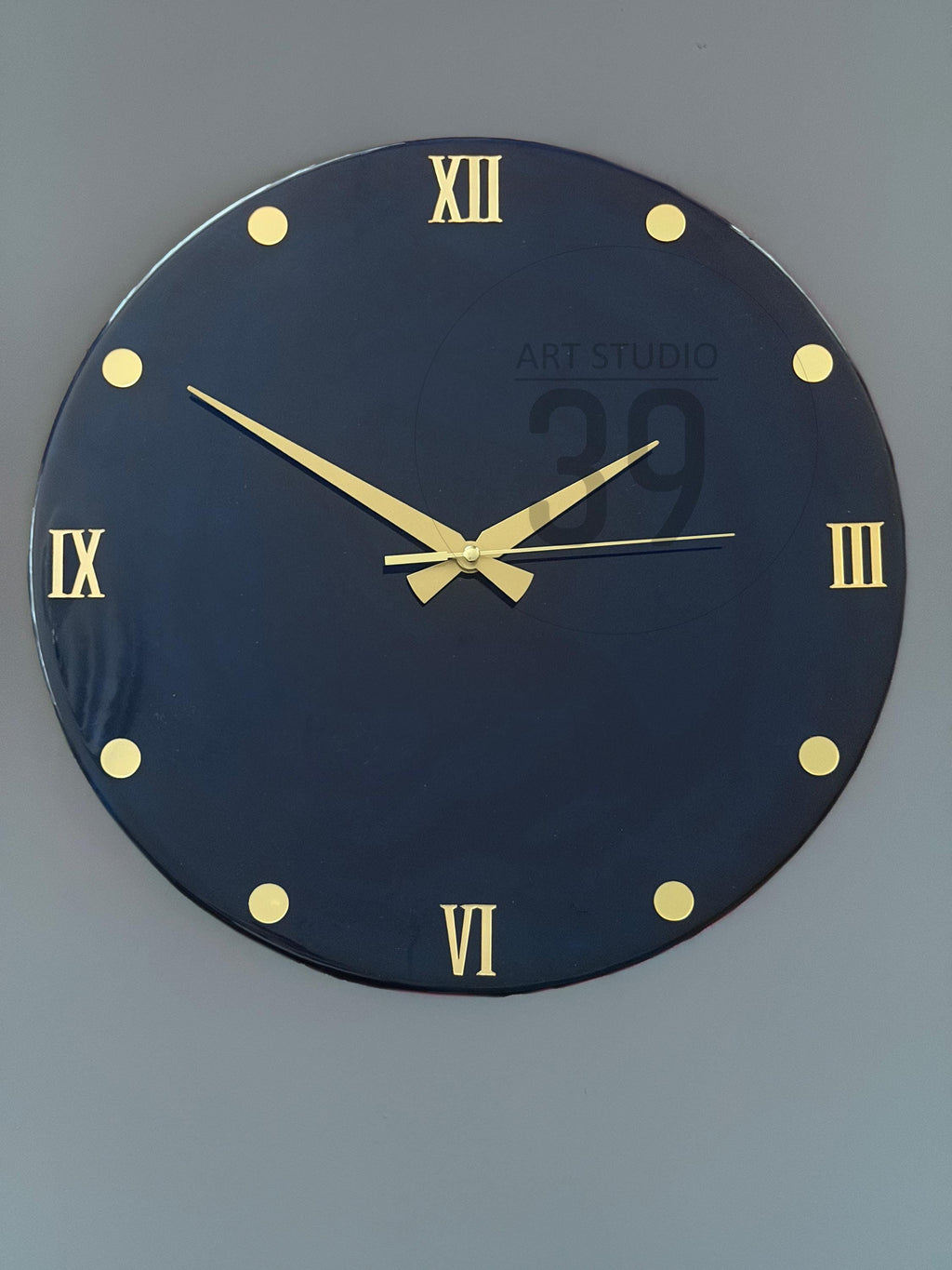A round, navy blue wall clock with gold-colored Roman numerals and hands. The clock face has gold-colored dot markers. The text "ART STUDIO 29" is printed on the clock face.
