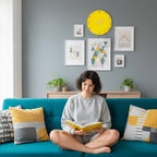 A woman sits on a teal sofa, reading a yellow book. The room features a yellow clock and framed art on a gray wall. Pillows with yellow and gray patterns accent the sofa. Plants and a wooden cabinet add to the decor.