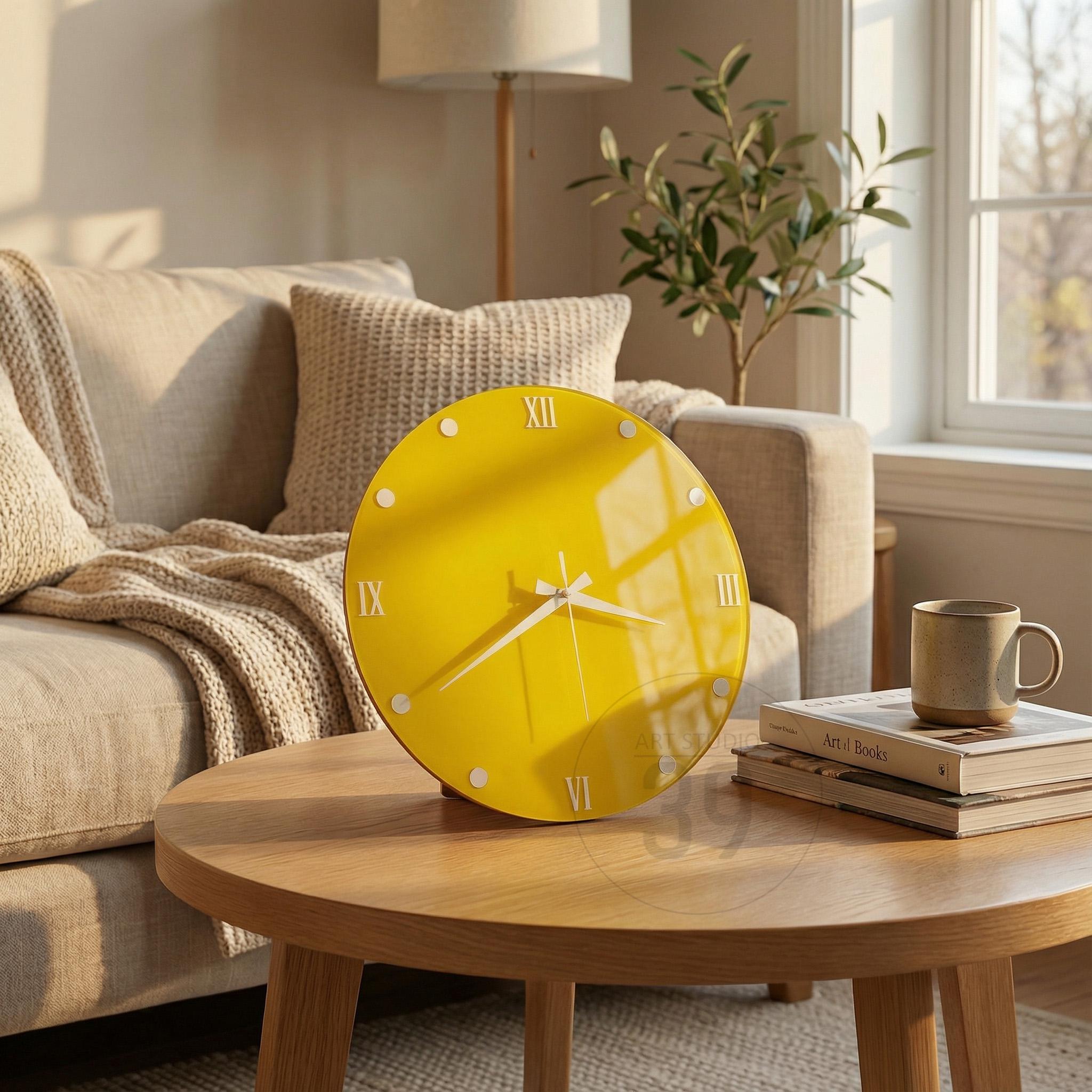 A round, yellow wall clock with white hands and Roman numerals. The clock is on a wooden table with a mug and books. The clock's face has a glossy finish and is surrounded by small white dots.