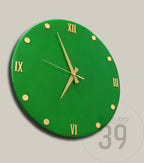 A round, green wall clock with gold-colored Roman numerals and hands. The clock face has gold-colored dots marking the hours. The clock is a modern design.