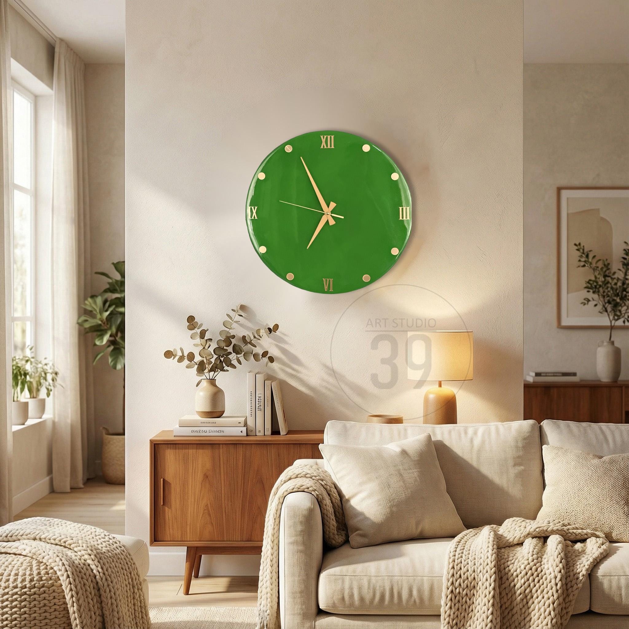 A round, green wall clock with gold-colored hands and Roman numeral hour markers. The clock is mounted on a light-colored wall. The clock's face is a solid green color. The clock is a decorative item for a living room.