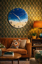 A round wall clock with a beach scene design. The clock face features a blue ocean, white waves, and a sandy beach. Roman numerals mark the hours. The clock is mounted on a patterned green and gold wallpaper.