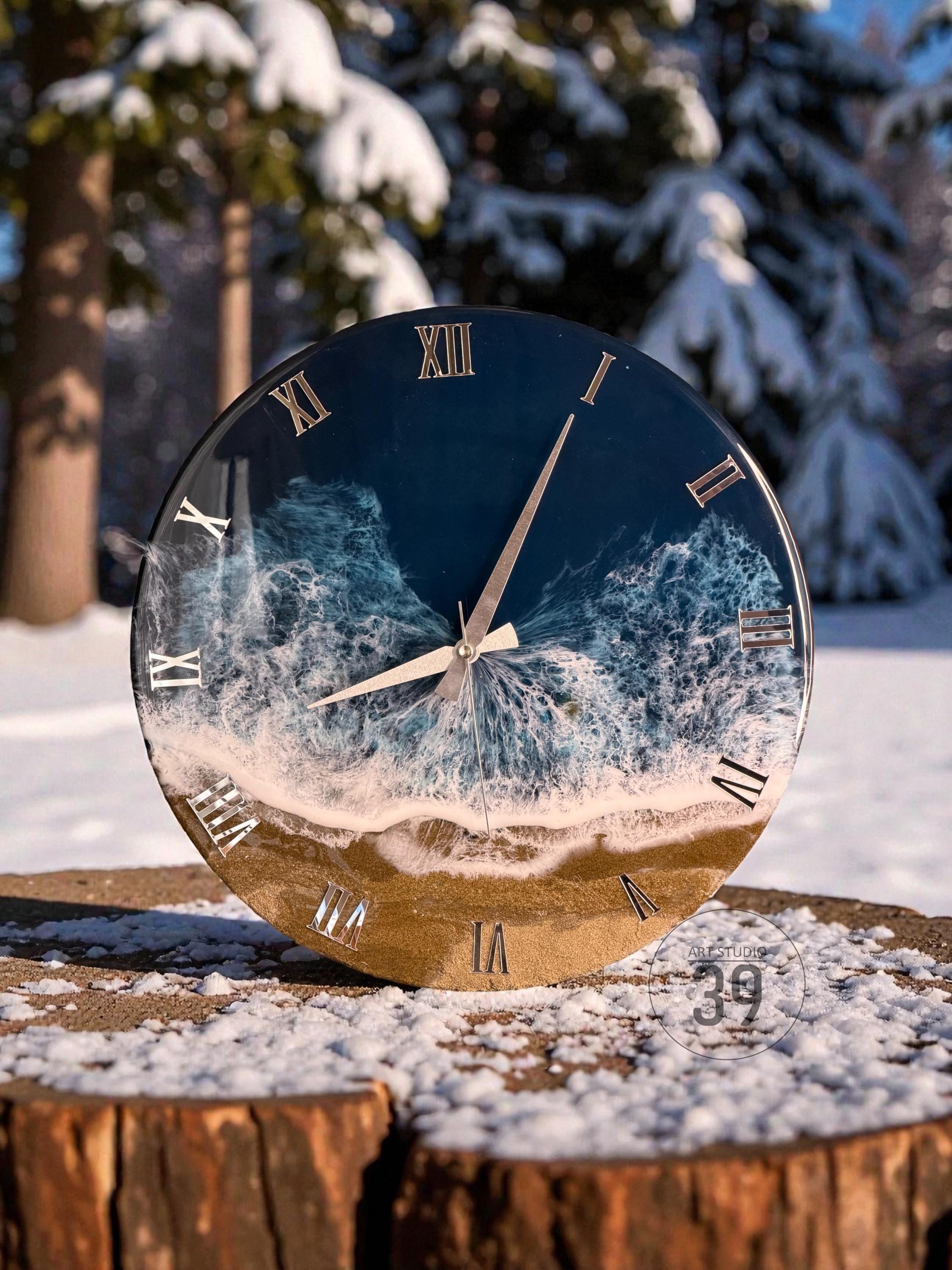 Round wall clock with a beach scene design. The clock face features a blue ocean, white waves, and a sandy shore. Roman numerals mark the hours. The clock hands are silver.