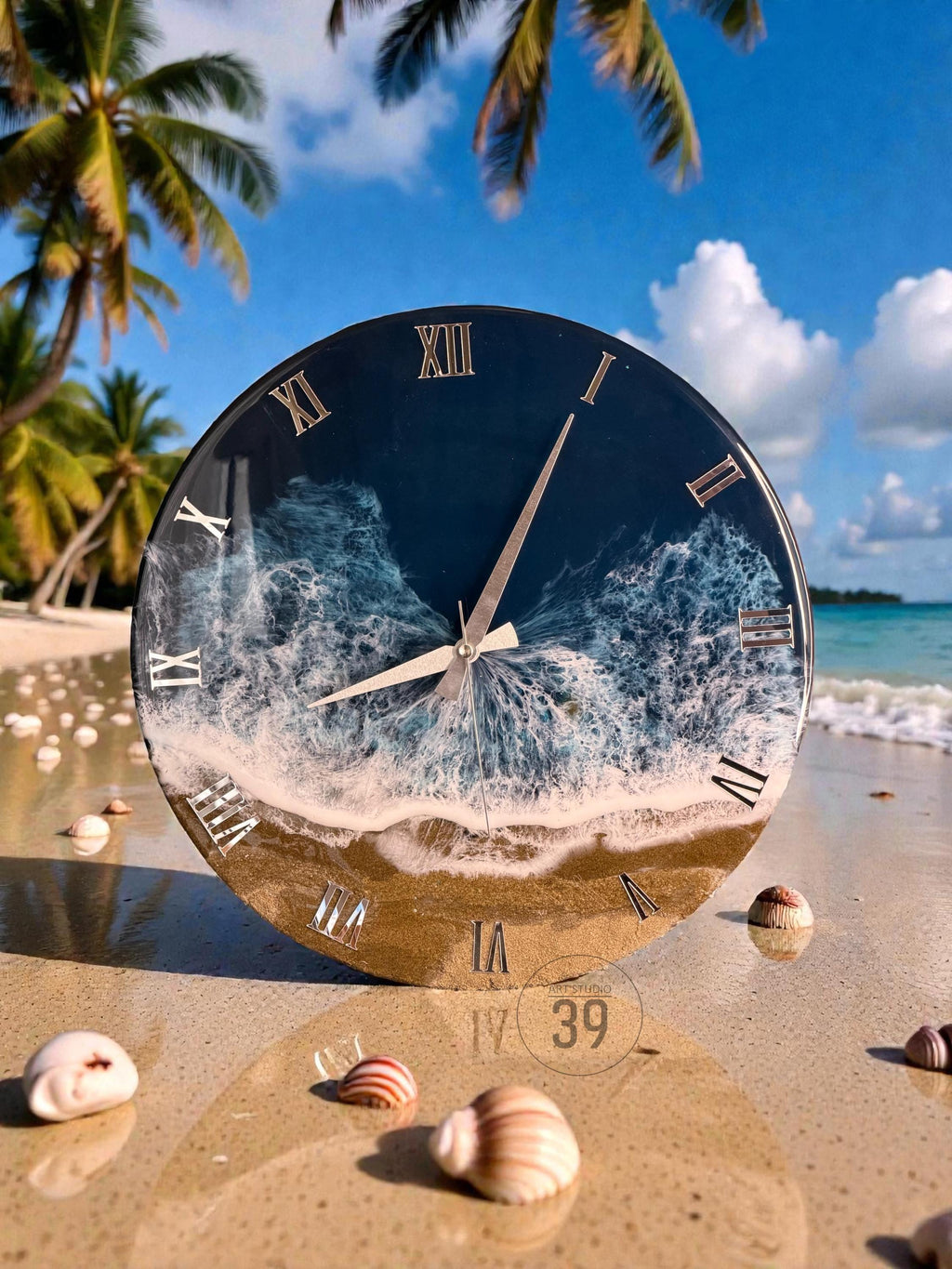 Round wall clock with a beach-themed design. The clock face features a dark blue ocean scene with white waves and a sandy shore. Roman numerals mark the hours. The clock is set on a sandy beach with seashells.