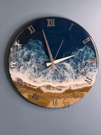 Round wall clock with a beach scene design. The clock face features a blue ocean with white waves, a sandy beach, and silver Roman numerals. The clock hands are silver.