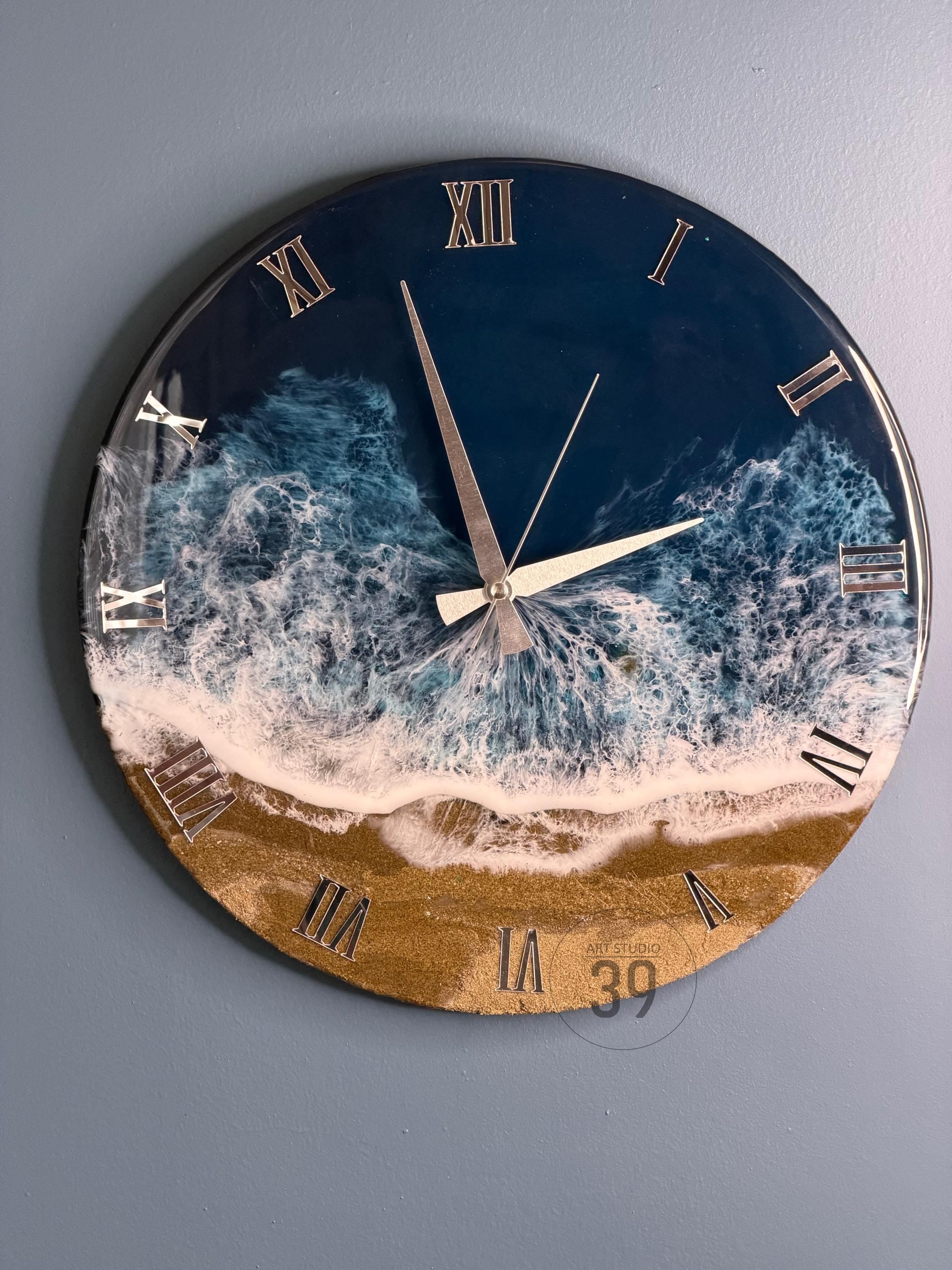 Round wall clock with a beach scene design. The clock face features a blue ocean with white waves, a sandy beach, and silver Roman numerals. The clock hands are silver.