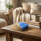 A decorative wooden box with a blue resin top, resembling ocean waves, rests on a rustic wooden coffee table. The box is surrounded by a stack of books and a coffee mug. The background includes a beige sofa and a small side table with a potted plant.