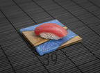 A piece of sushi with a bright red tuna topping sits atop a wooden and blue resin serving board. The board is square and rests on a dark, textured surface. The image includes the text "ART STUDIO 39".