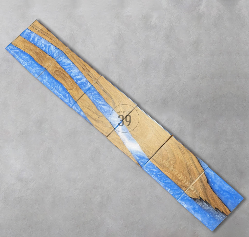 A rectangular wooden art piece with a river-like design. The wood has a natural grain, with sections of blue resin flowing through it. The text "ART STUDIO 39" is visible.