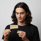 A rectangular wooden object with a light-colored wood top and a dark, marbled bottom. The object is being held up by a person wearing a black t-shirt. The background is a plain white.