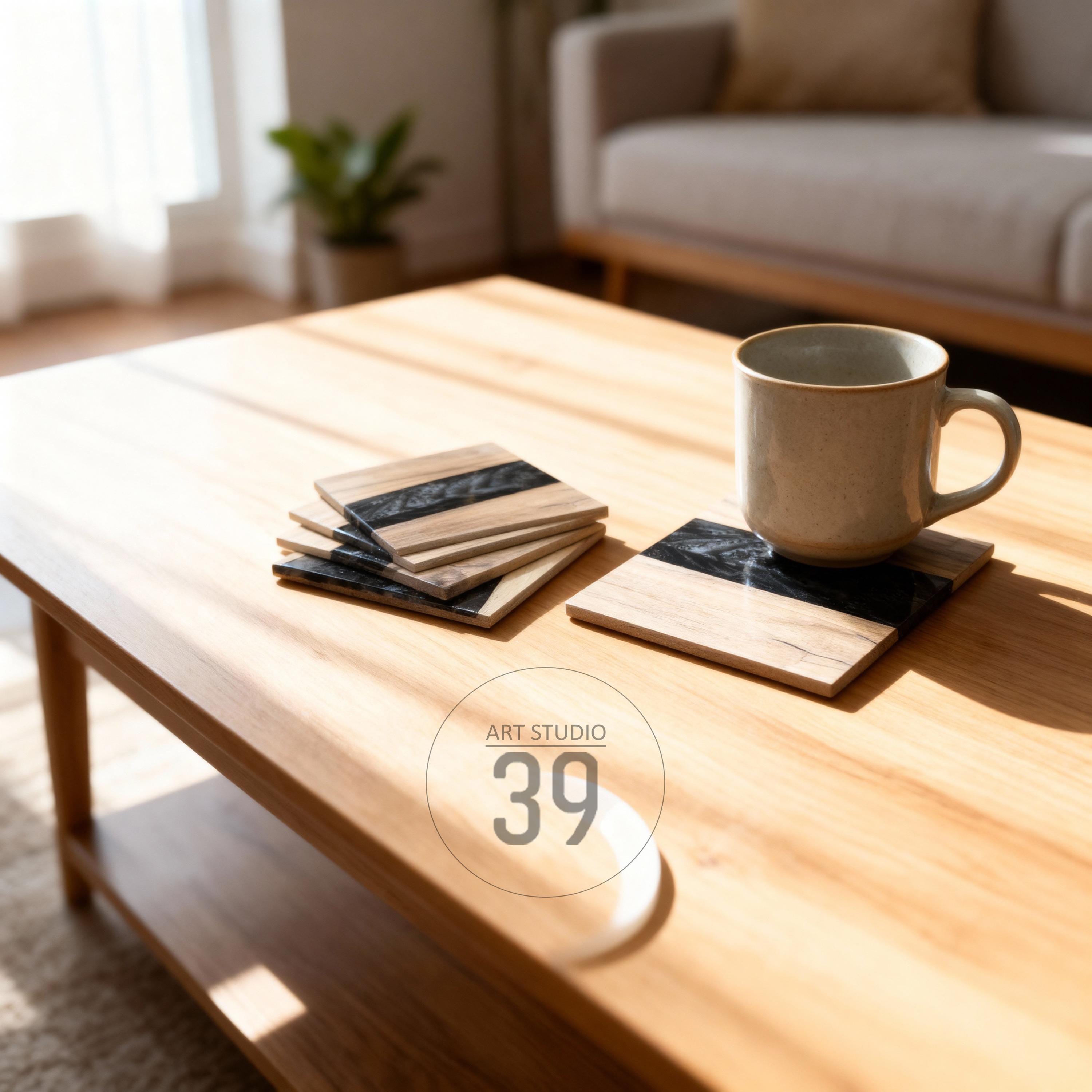 Wooden coasters with a black resin stripe and a coffee mug on a wooden table. The coasters have a natural wood grain pattern. The text "ART STUDIO 39" is in a circle on the table.