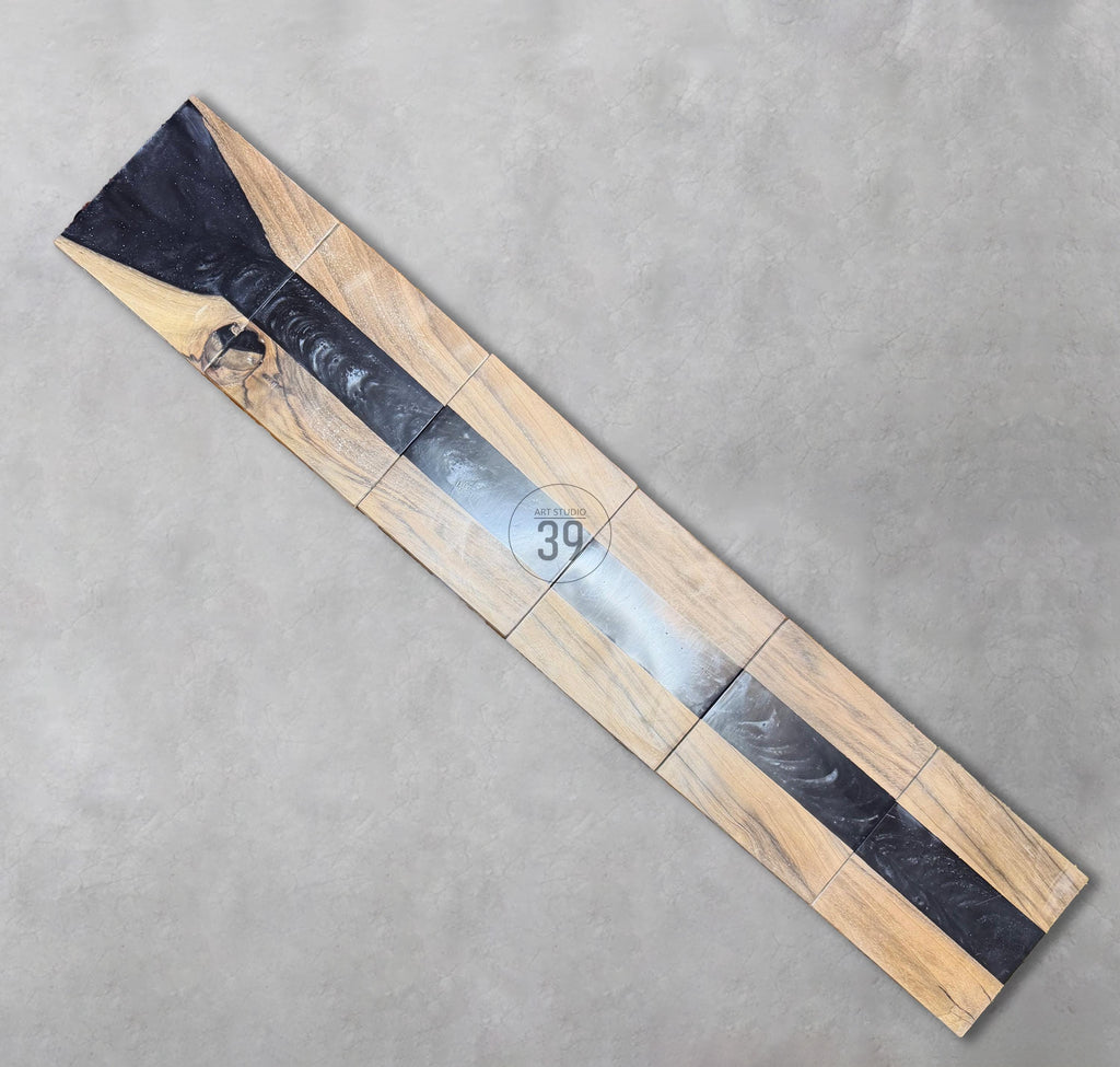 A rectangular wooden table with a dark gray epoxy resin river. The table is made of several wooden blocks with a natural wood grain pattern. The epoxy river runs down the center. The text "ART STUDIO 39" is in the center.