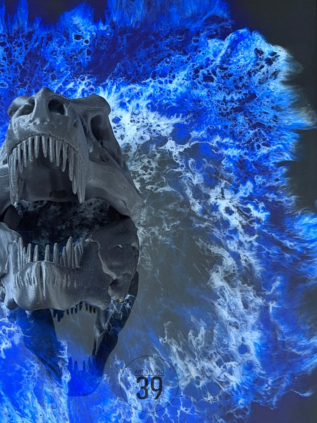 A dark gray dinosaur skull with sharp teeth is set against a vibrant blue and white abstract background. The artwork features the text "ART STUDIO 39" in a circular design. The overall theme is prehistoric art.