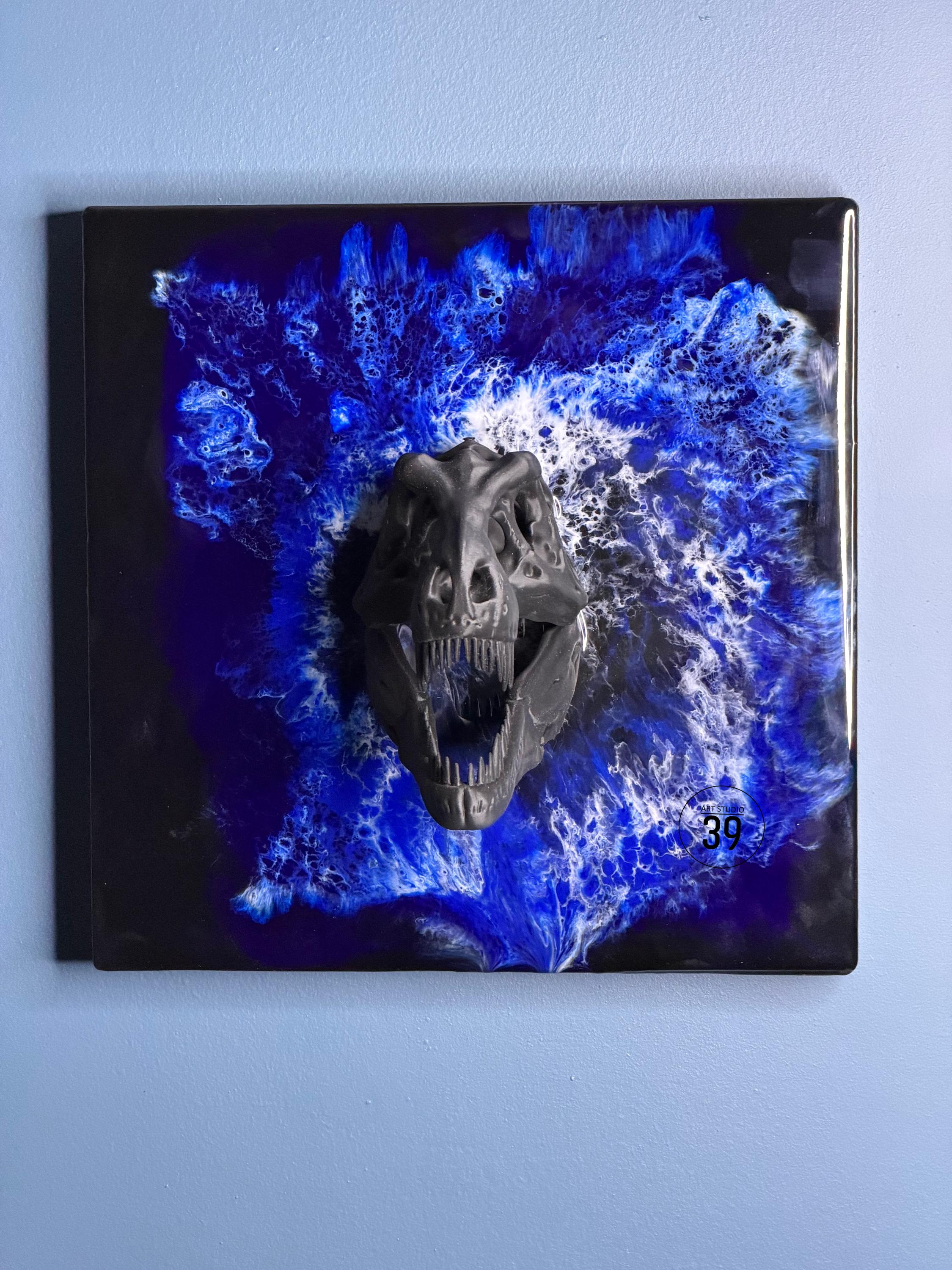 A black Tyrannosaurus Rex skull sculpture mounted on a square black background with a blue and white abstract design. The sculpture is three-dimensional and has detailed features.