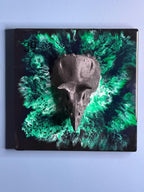 A square, black resin art piece featuring a dark gray bird skull. The skull is centered against a swirling background of green and black resin. The number "39" is visible in the upper left corner.