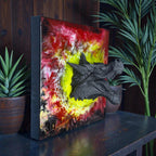 A square wall art piece featuring a black dragon head emerging from a vibrant background of red, yellow, and white swirls. The artwork has a black frame and a logo in the bottom left corner.