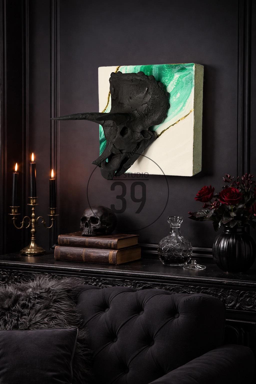 A black triceratops skull sculpture mounted on a white and green canvas with gold accents. The scene includes a black skull, books, candles, and a vase of red roses, creating a gothic aesthetic.