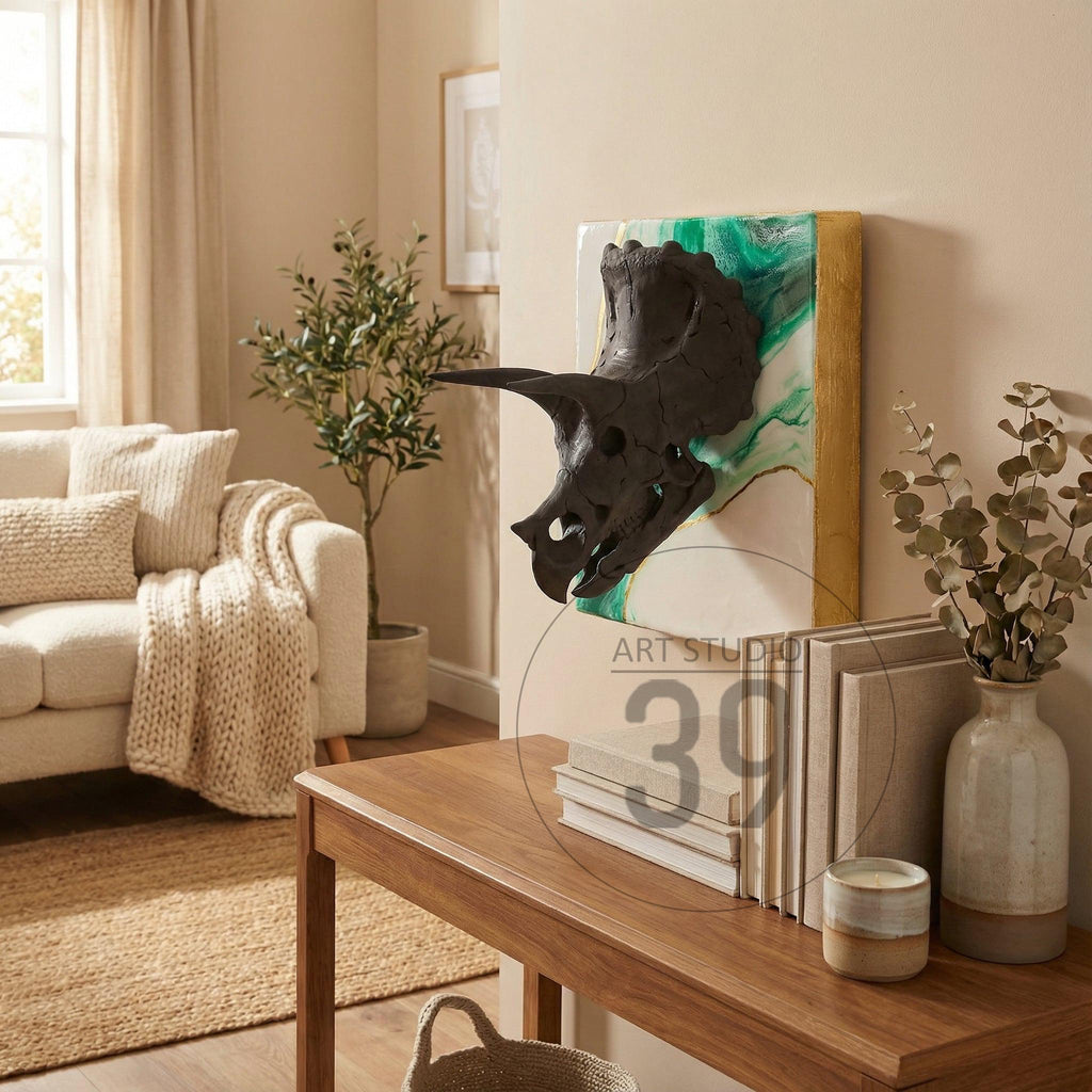A black triceratops skull sculpture mounted on a white and green background with a gold frame. The artwork is displayed on a beige wall in a living room setting. The text "ART STUDIO 39" is visible.