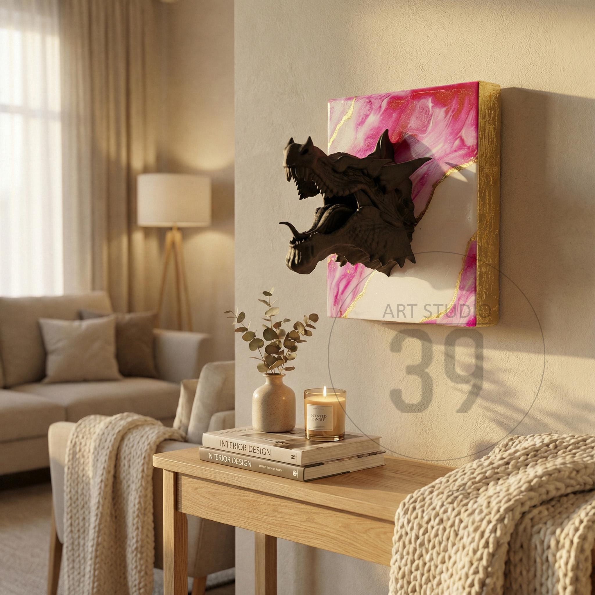 A dark bronze dragon head sculpture mounted on a canvas with pink and gold abstract art. The artwork is displayed on a wall in a living room setting. The text "ART STUDIO" and the number "39" are visible.