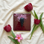 A square, burgundy-colored art piece with a black bird skull in the center. The background has a splash of pink and white. The image is decorated with red tulips and a pink flower. The text "ART STUDIO 39" is in the bottom right corner.
