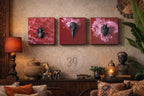 Three square wall art pieces with dark red backgrounds. One features a black spider, another a bird skull, and the third a heart. The art is displayed above a dark wooden cabinet with decorative items.