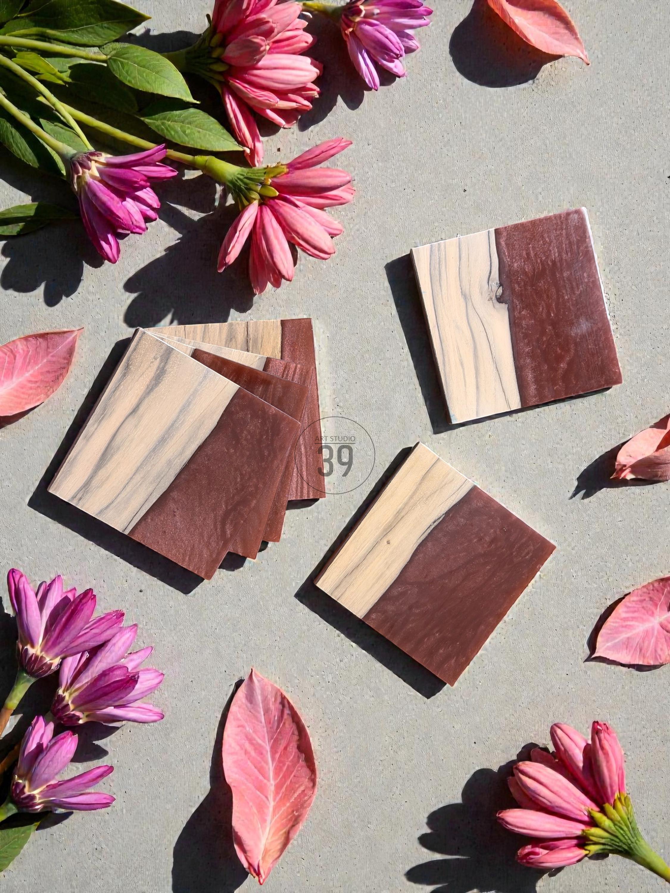 Square wooden coasters with a two-tone design, featuring a light wood grain and a dark brown section. The coasters are arranged with pink flowers and leaves on a gray surface. The image includes the text "ST STUDIO 39".