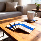 Wooden coasters with a blue resin stripe. A white mug sits on one coaster, with others stacked nearby. The coasters are on a wooden table, with a couch and plant in the background. The coasters have the number "39" on them.