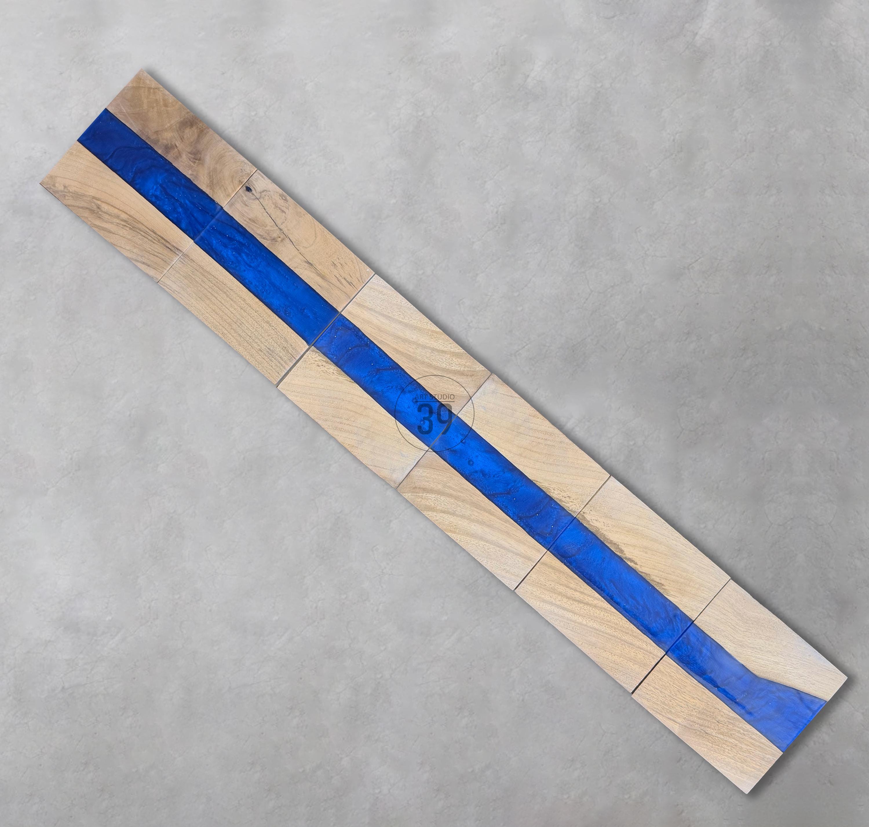 Wooden decorative piece with a vibrant blue resin river running through the center. The wood is light-colored, and the resin is a deep blue. The number "39" is visible on the wood. The piece is made of several rectangular blocks.