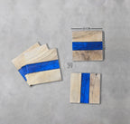 Set of four square wooden coasters. Each coaster is 12 cm x 12 cm (4.7 inches x 4.7 inches) with a vibrant blue resin stripe. The coasters have a natural wood grain finish, adding a rustic touch to any home decor.