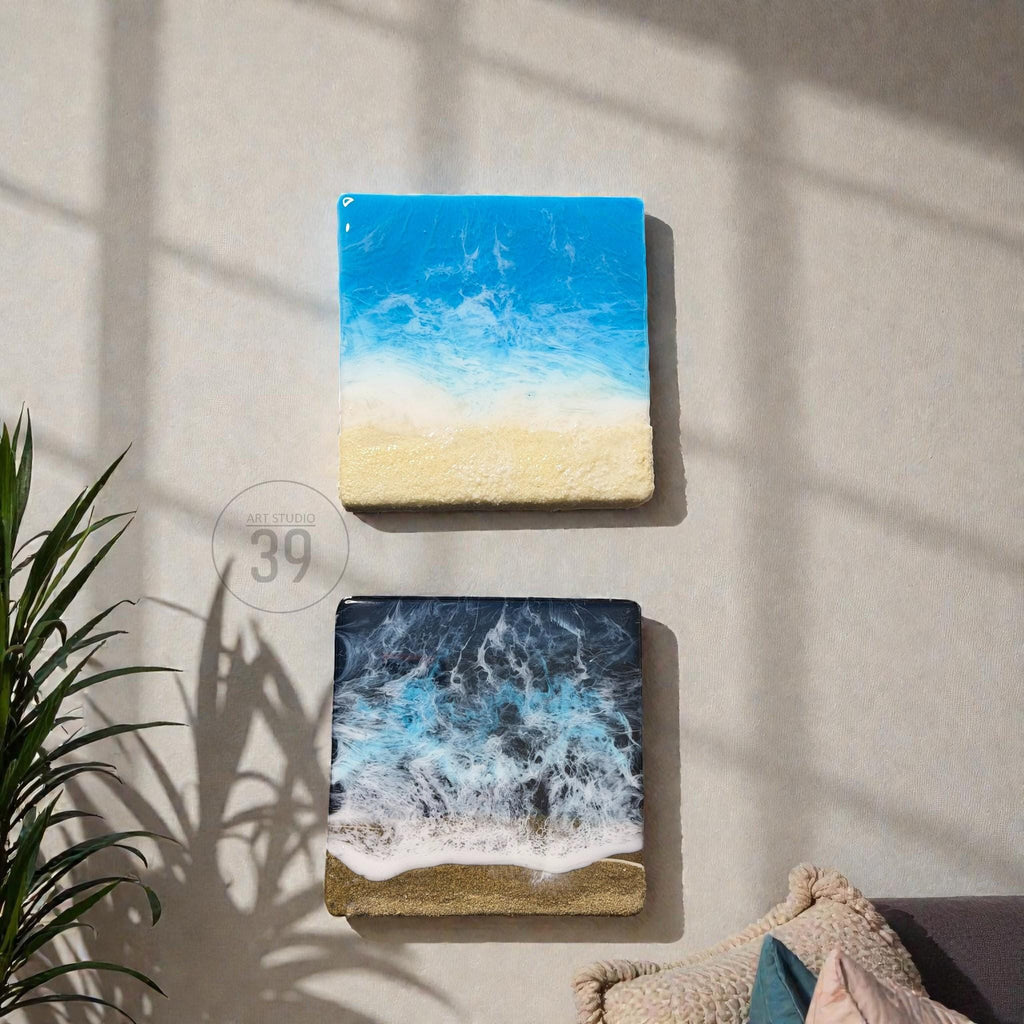 Two square resin art pieces depicting ocean scenes. The top piece shows a bright blue sky and white waves over a sandy beach. The bottom piece has a dark blue ocean with white foamy waves and a sandy shore. The text "ART STUDIO 39" is in the center.