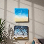 Two square resin art pieces depicting ocean scenes. The top piece shows a bright blue sky and white waves over a sandy beach. The bottom piece has a dark blue ocean with white foamy waves and a sandy shore. The text "ART STUDIO 39" is in the center.
