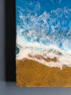 Abstract artwork depicting a beach scene with a golden sand shore and foamy white waves crashing against a bright blue ocean. The artwork has a textured appearance and a small circular logo with the number 39.
