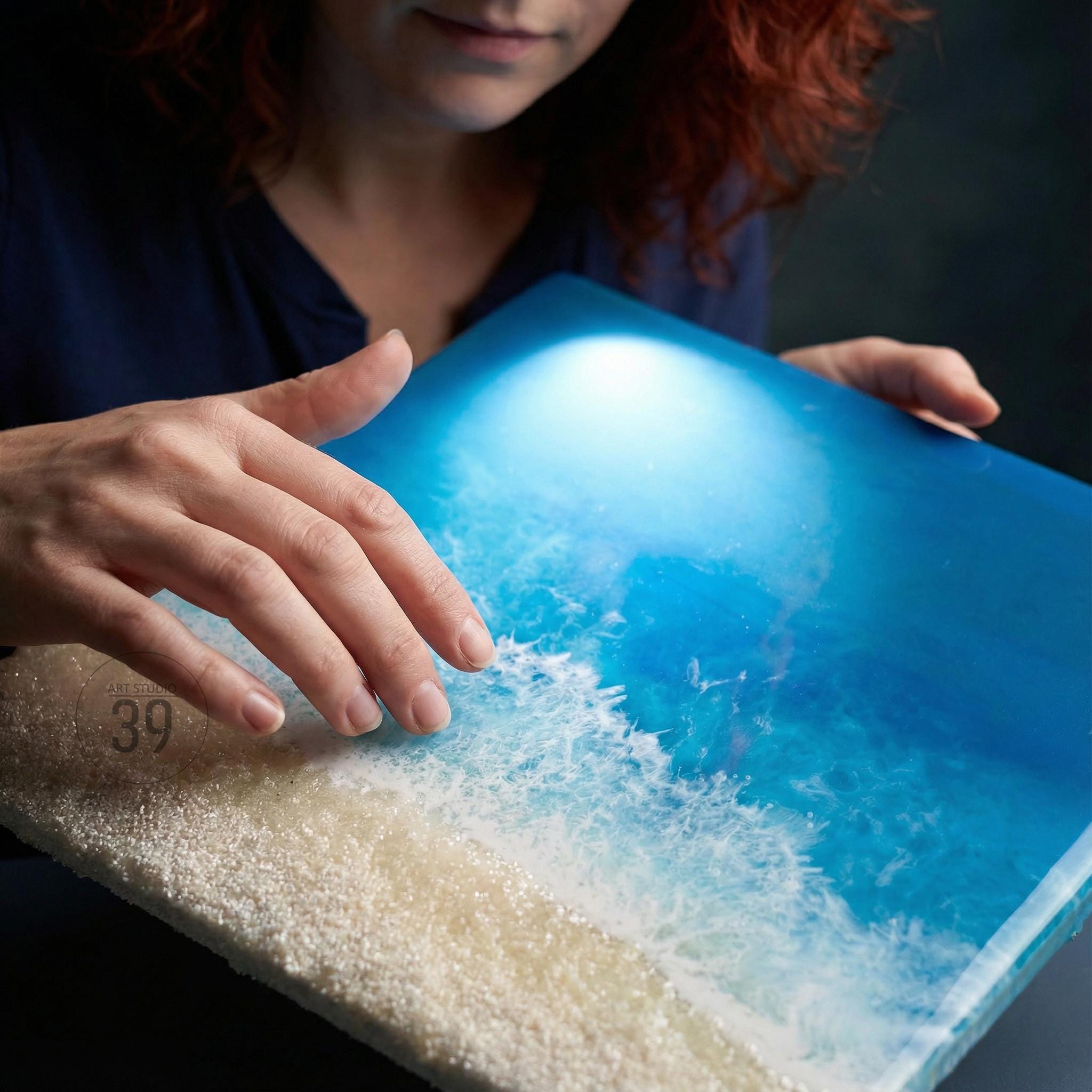 A rectangular resin art piece depicting an ocean scene with a sandy beach. The artwork features shades of blue and white, with a textured wave effect. The beach area is made of small, granular material. The number "39" is visible on the edge.