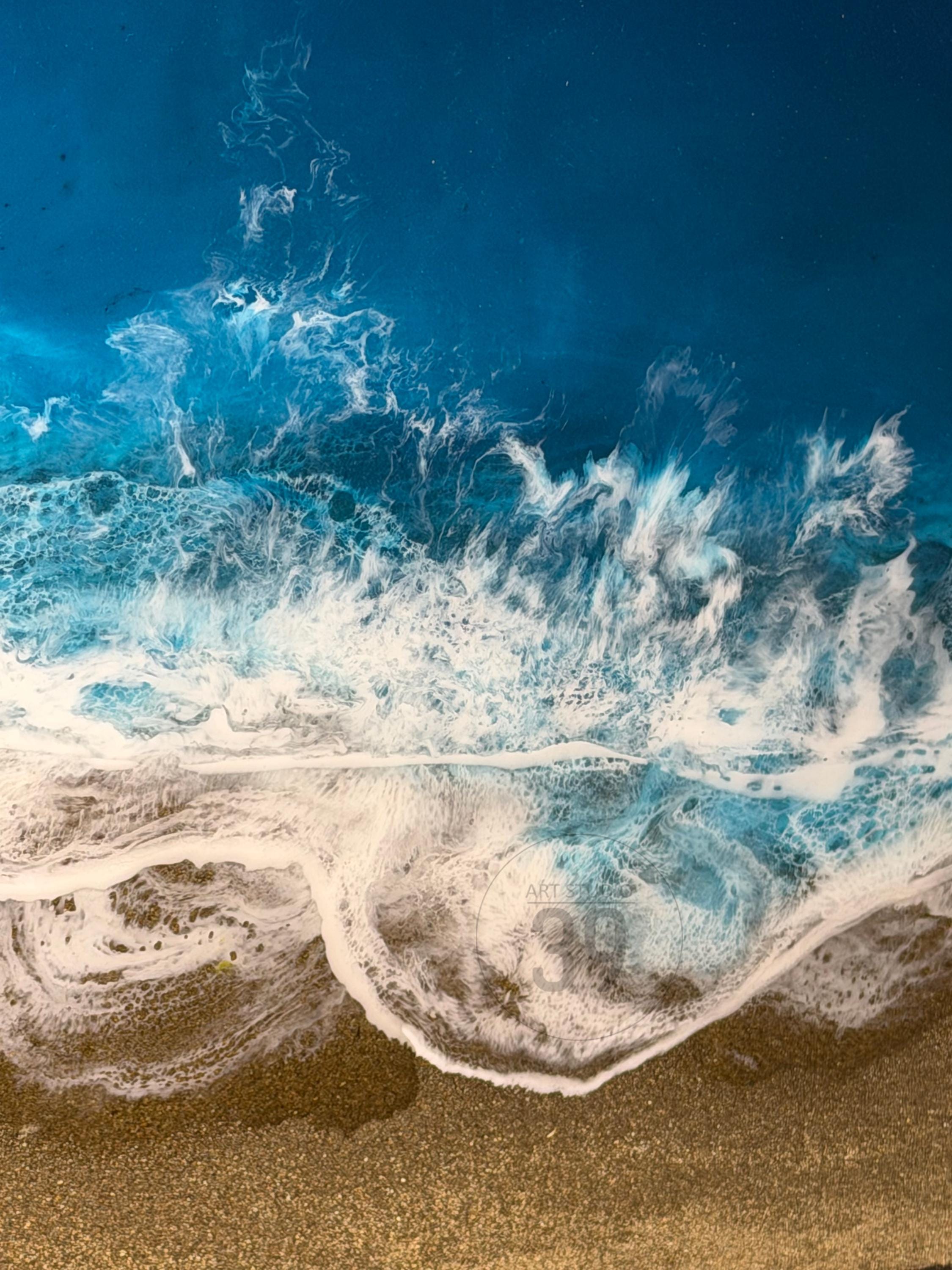 Abstract ocean art piece featuring a vibrant depiction of waves crashing onto a sandy shore. The artwork showcases shades of deep blue, turquoise, and white, with a textured effect to simulate the ocean's movement. The sandy beach is a warm tan color.