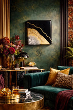 A luxurious living room with a dark green velvet sofa and gold accents. A black and gold abstract art piece hangs on the wall. Decorative pillows in gold and leopard print add texture. A gold-trimmed table holds a lamp and books.