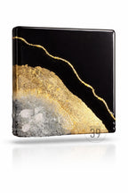 Square resin art piece with a black background, gold leaf accents, and a textured, crystal-like base. The gold leaf forms a diagonal line across the black surface. The bottom edge features a rough, crystal-like texture.