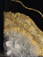 Abstract art piece featuring a black background with a gold leaf design. The artwork incorporates clear quartz crystals and glitter accents. The piece has a layered texture and a modern aesthetic.