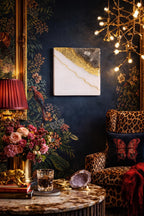 A square wall art piece with a white background and gold and gray accents hangs on a dark blue floral wallpapered wall. A red lampshade and a leopard print armchair are also visible.