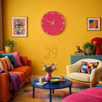 A vibrant living room with a yellow wall, featuring a magenta clock, colorful artwork, and an orange sofa with patterned pillows. A blue coffee table holds a pink vase and striped mugs. The room has a modern, eclectic style.