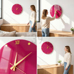 A round, magenta wall clock with gold-colored hands and hour markers. The clock has a glossy finish and features Roman numerals at the top and bottom. The clock is mounted on a white wall.
