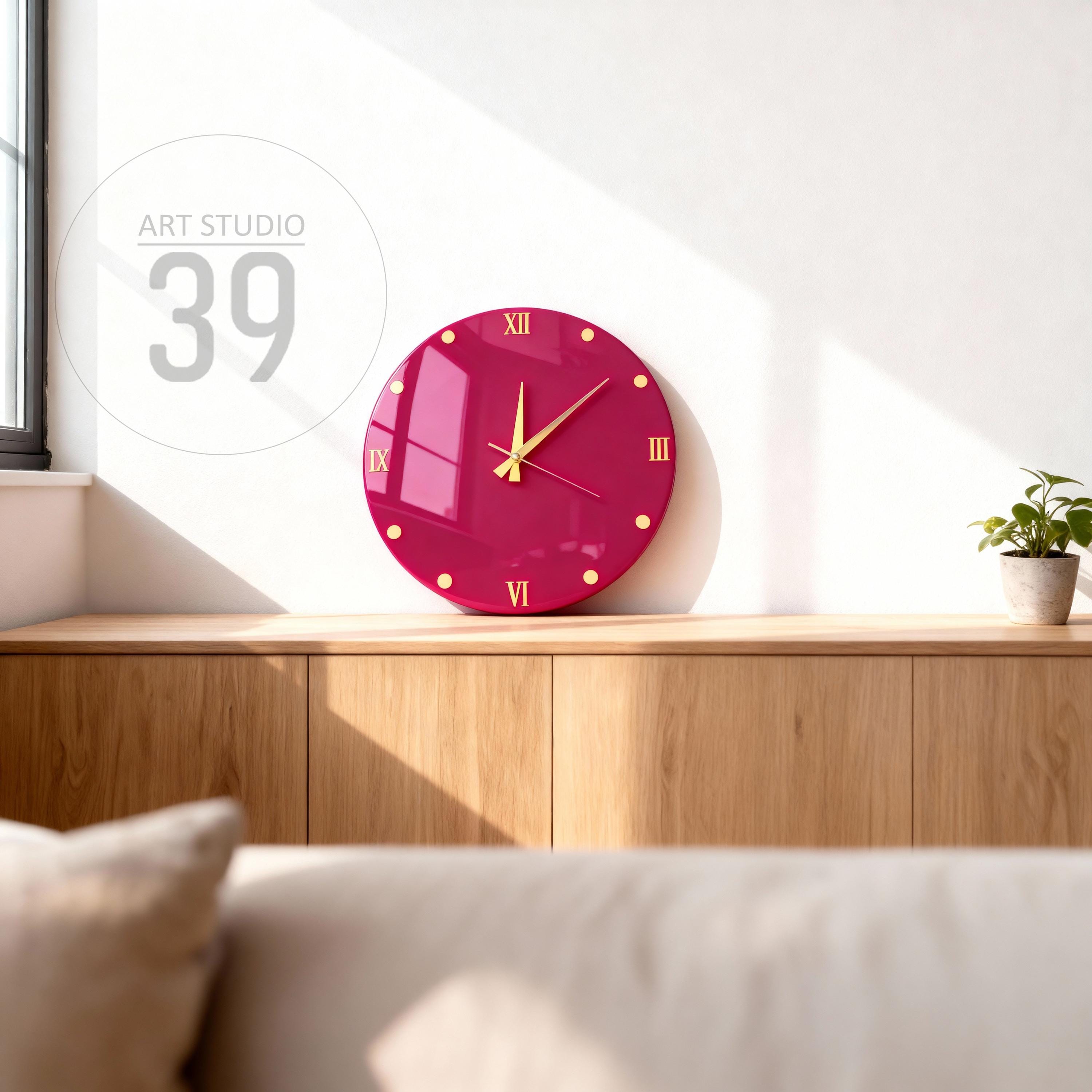 A round, magenta wall clock with gold-colored hands and hour markers. The clock features Roman numerals at the 12, 3, 6, and 9 o'clock positions. The text "ART STUDIO 39" is in the upper left corner.