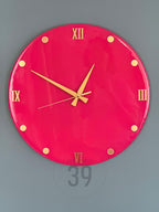 A round, hot pink wall clock with gold-colored hands and Roman numeral hour markers. The clock has gold-colored dots marking the hours and the text "ART STUDIO 39" is visible at the bottom.