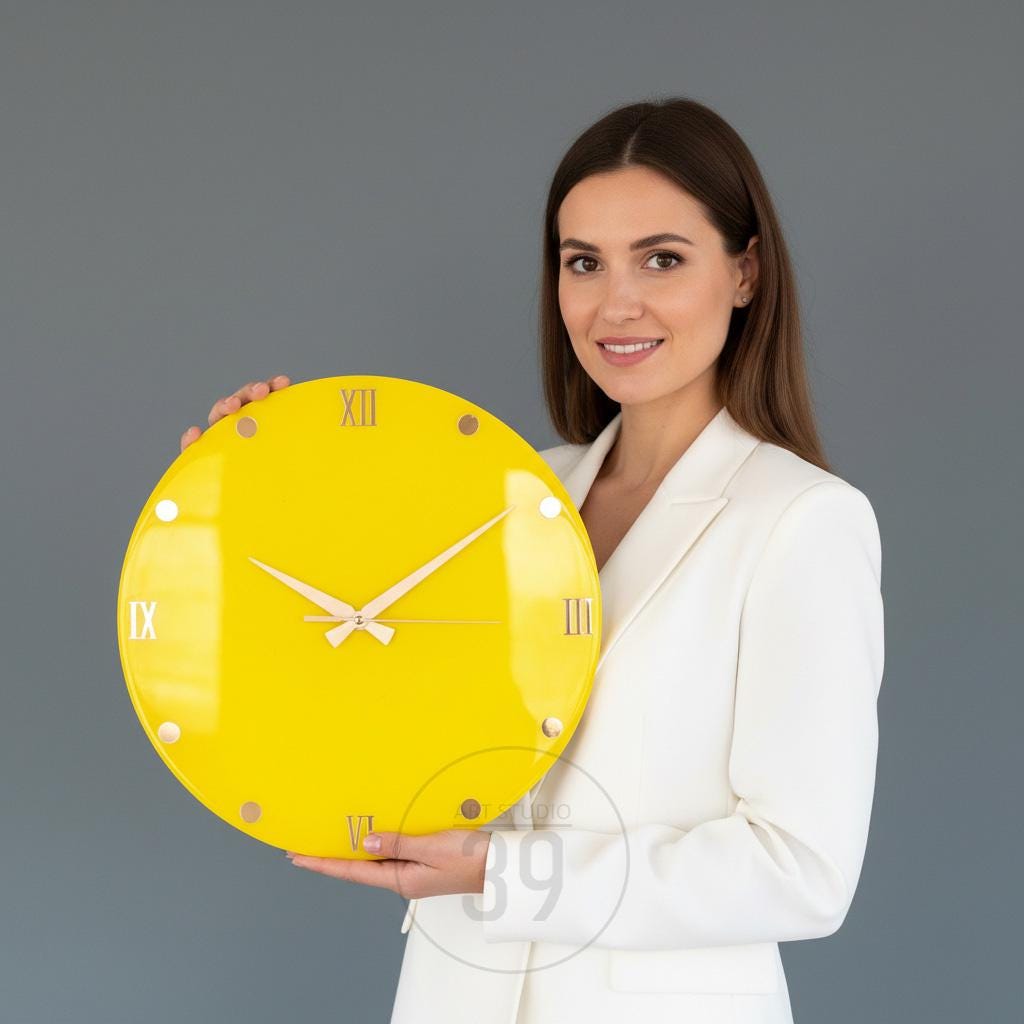 A bright yellow, round wall clock with Roman numerals and gold-colored hands. The clock is held in front of a person wearing a white blazer. The clock's face is a solid, vibrant yellow.