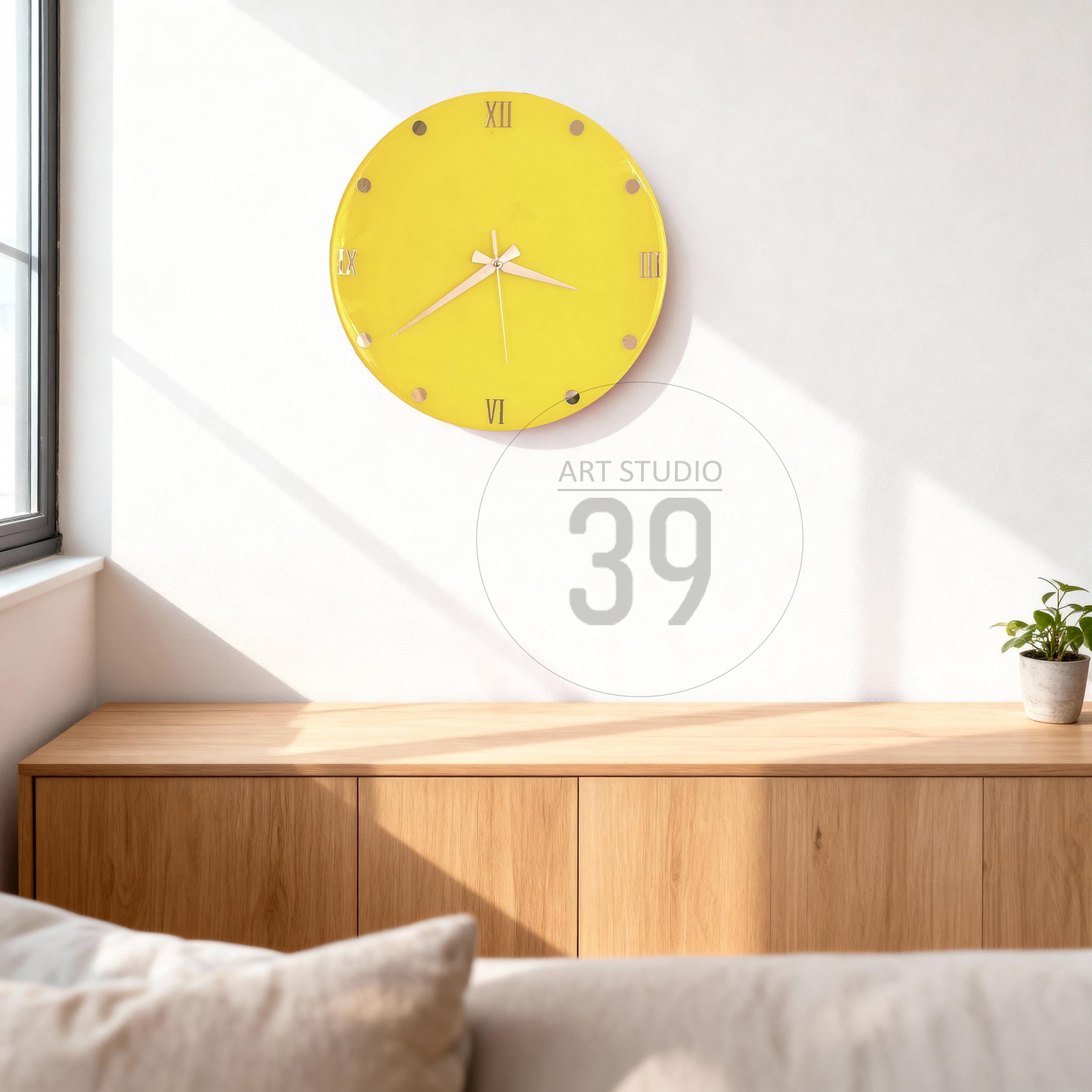 A round, yellow wall clock with Roman numerals and gold-colored accents. The clock hands are white. The clock is mounted on a white wall. The image also includes the text "ART STUDIO 39".
