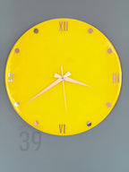 A round, bright yellow wall clock with gold-colored Roman numerals and hands. The clock face has gold-colored dots marking the hours. The clock reads 6:10. The text "ART STUDIO 39" is visible on the bottom left.