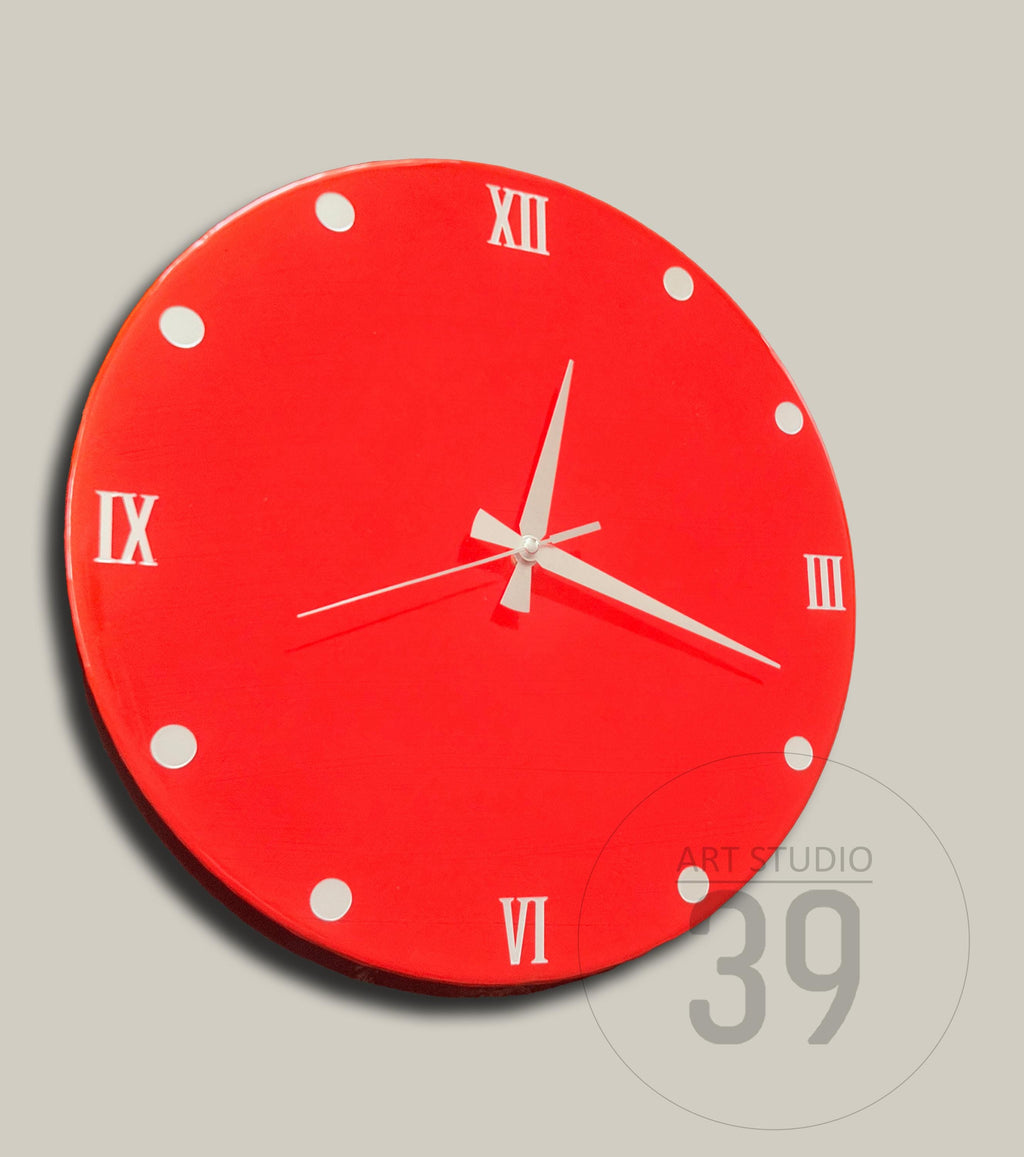 A round, red wall clock with white Roman numerals and hands. White dots mark the hours. The clock face has a glossy finish. The clock is a decorative item for home decor.
